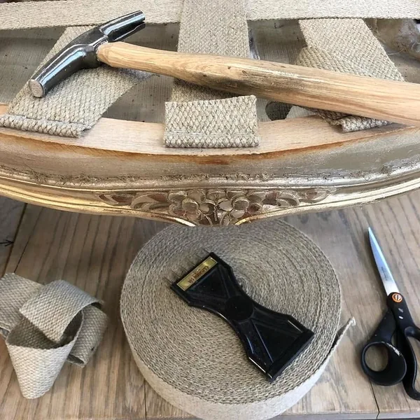 Sur l'établi : marteau de tapissier, rouleaux de sangle, tendeur et ciseaux